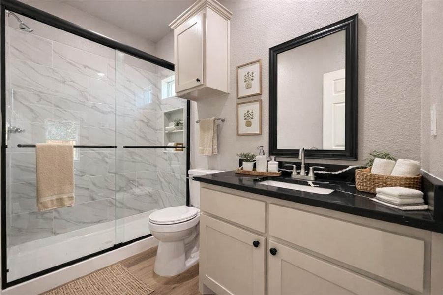 Bathroom featuring vanity, a marble finish shower, a textured wall, and light wood-style flooring