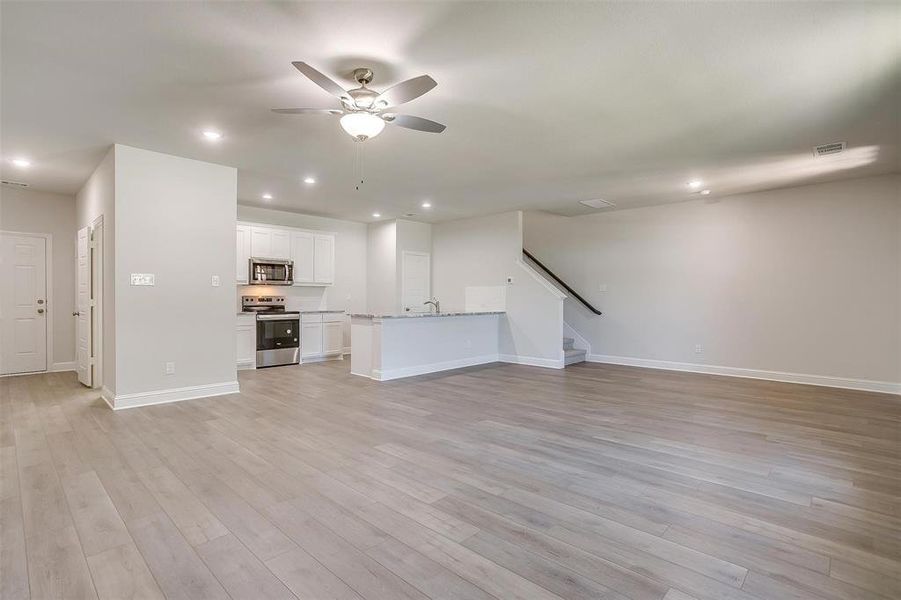 Unfurnished living room with light wood-type flooring, recessed lighting, ceiling fan, and stairway Unfurnished living room with light wood-type flooring, recessed lighting, ceiling fan, and stairway