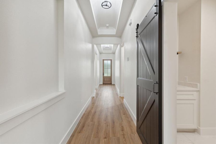 Hall with baseboards, a barn door, light wood-style flooring, and a raised ceiling