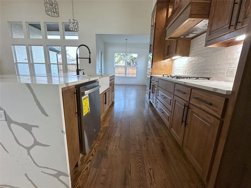 Kitchen with sink, custom exhaust hood, hanging light fixtures, a center island with sink, and appliances with stainless steel finishes