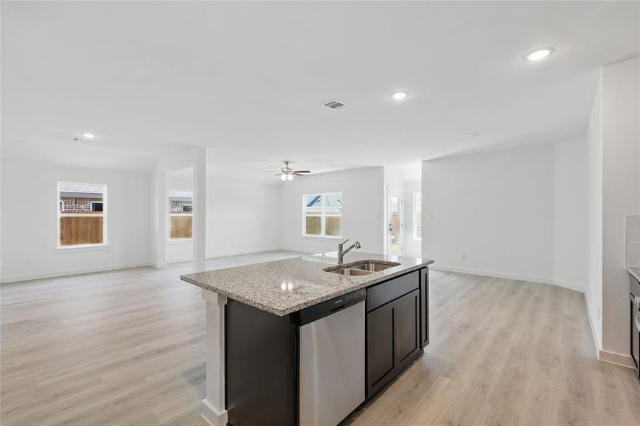 Kitchen featuring open floor plan, an island with sink, dishwasher, light stone countertops, and light wood finished floors