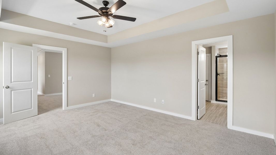 Bedroom with tray ceiling, windows, and en-suite primary bathroom