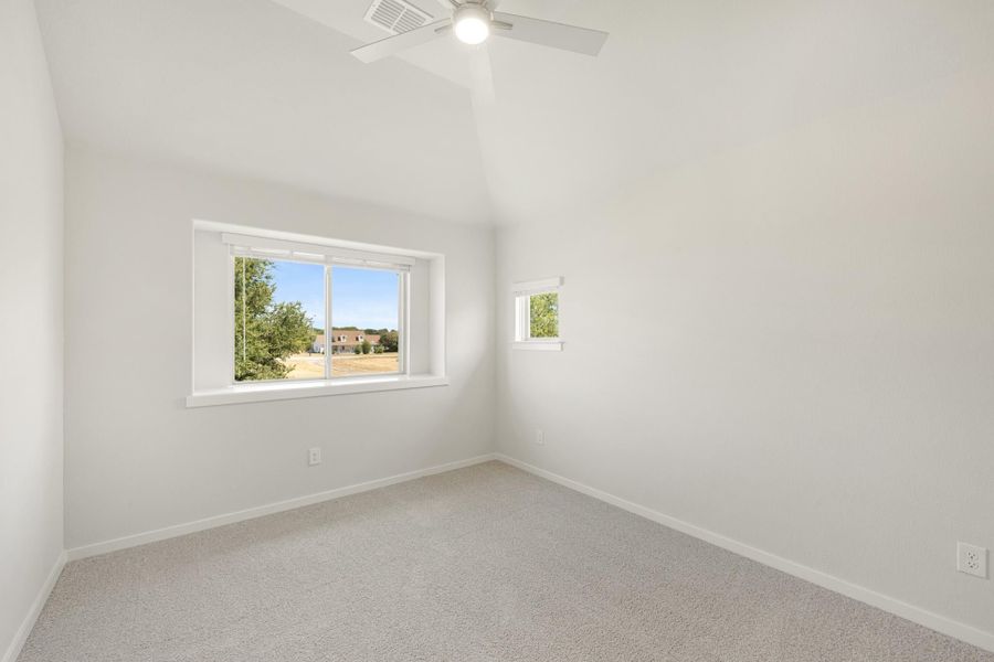 Empty bedroom with vaulted ceiling, ceiling fan, carpet flooring, and two windows with outdoor views