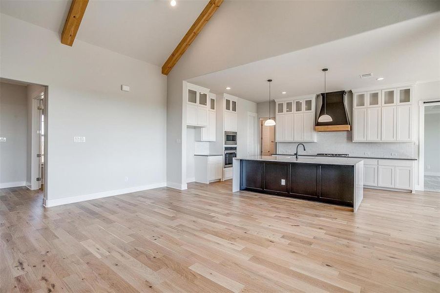 Kitchen with beamed ceiling, hanging light fixtures, light hardwood / wood-style floors, a kitchen island with sink, and custom range hood