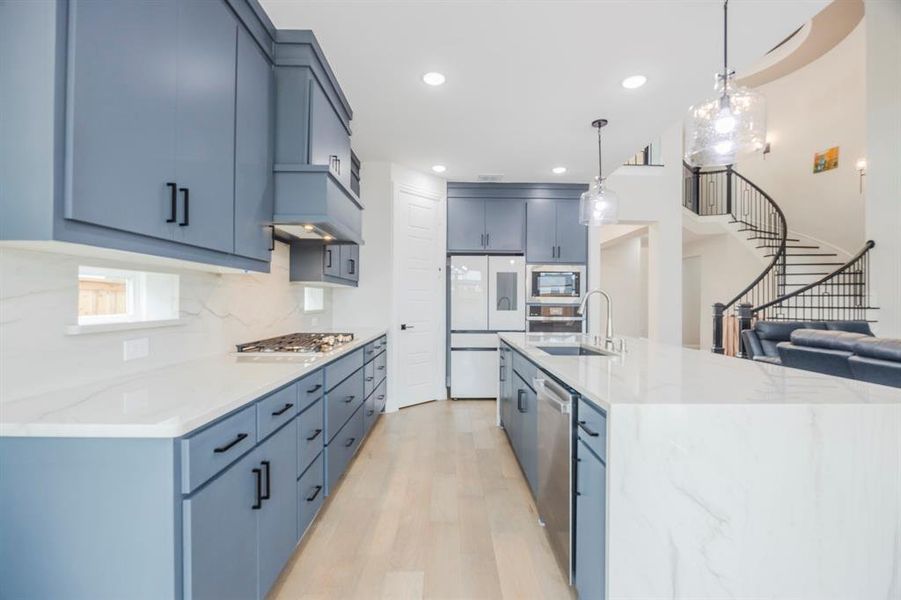 Kitchen with backsplash, light stone counters, light wood-style floors, stainless steel appliances, and a sink