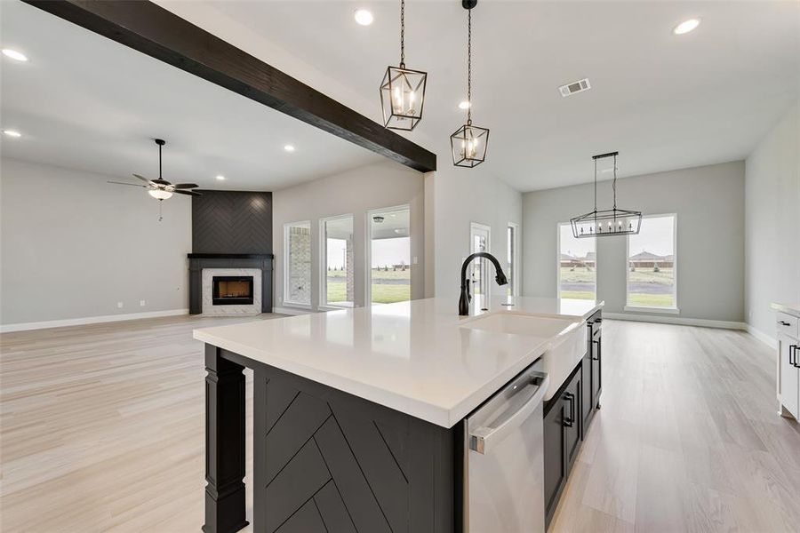 Kitchen with dishwasher, a center island with sink, plenty of natural light, and a large fireplace