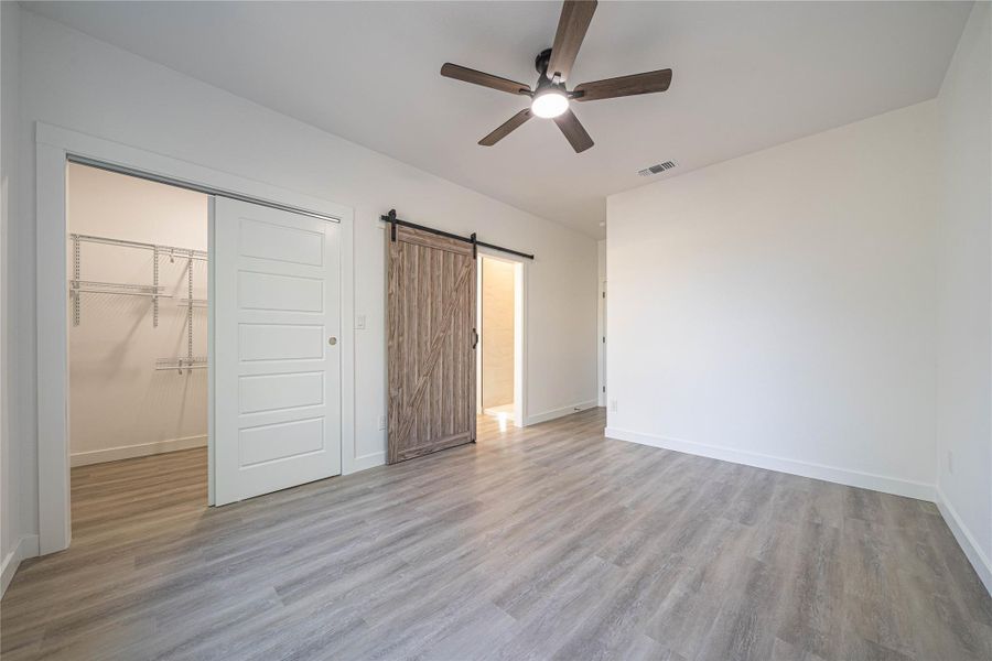 Unfurnished bedroom with a barn door, a ceiling fan, light wood-style flooring, and a spacious closet
