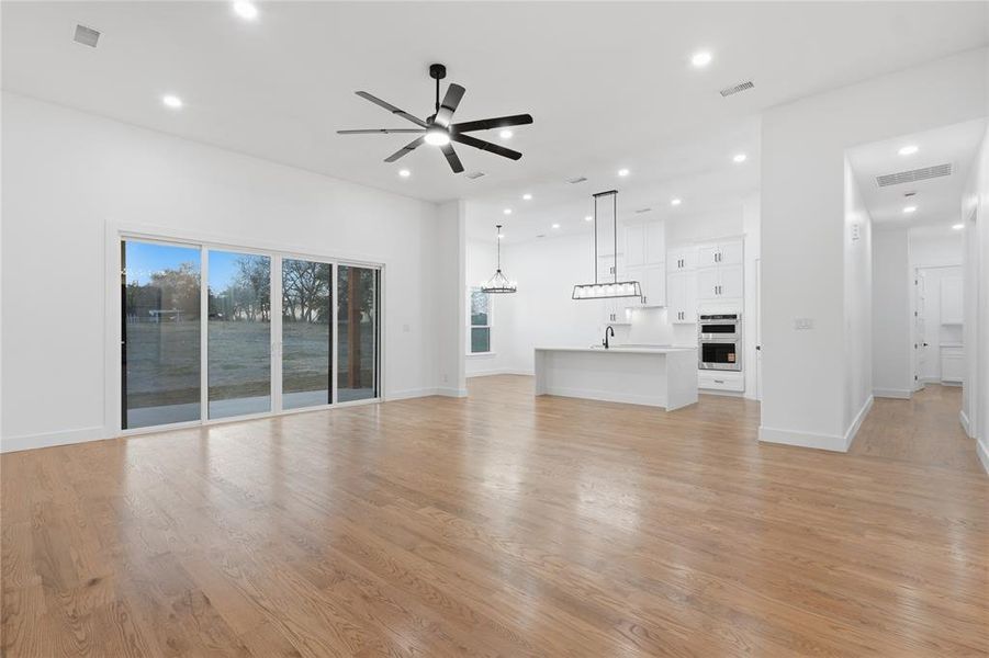 Unfurnished living room with ceiling fan, light wood-style floors, and suspended lighting