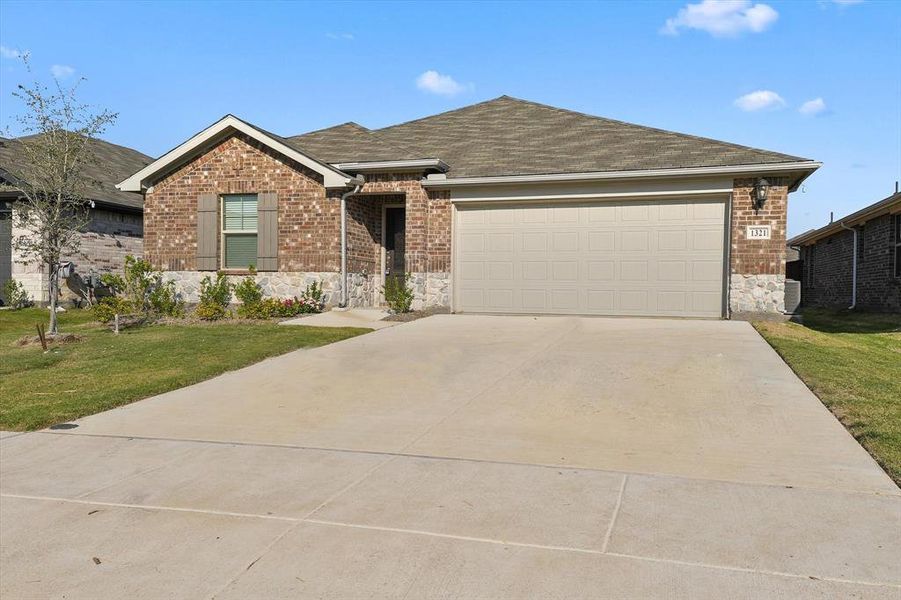 Single story home featuring stone siding, driveway, a front yard, an attached garage, and a shingled roof Single story home featuring stone siding, driveway, a front yard, an attached garage, and a shingled roof