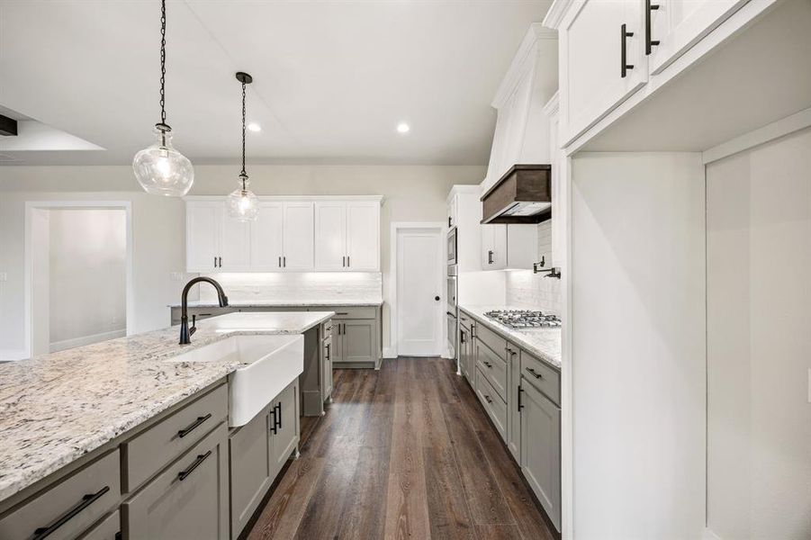 Two tone kitchen featuring backsplash, hanging light fixtures, dark wood finished floors, dual tone cabinetry, and light stone counters Two tone kitchen featuring backsplash, hanging light fixtures, dark wood finished floors, dual tone cabinetry, and light stone counters