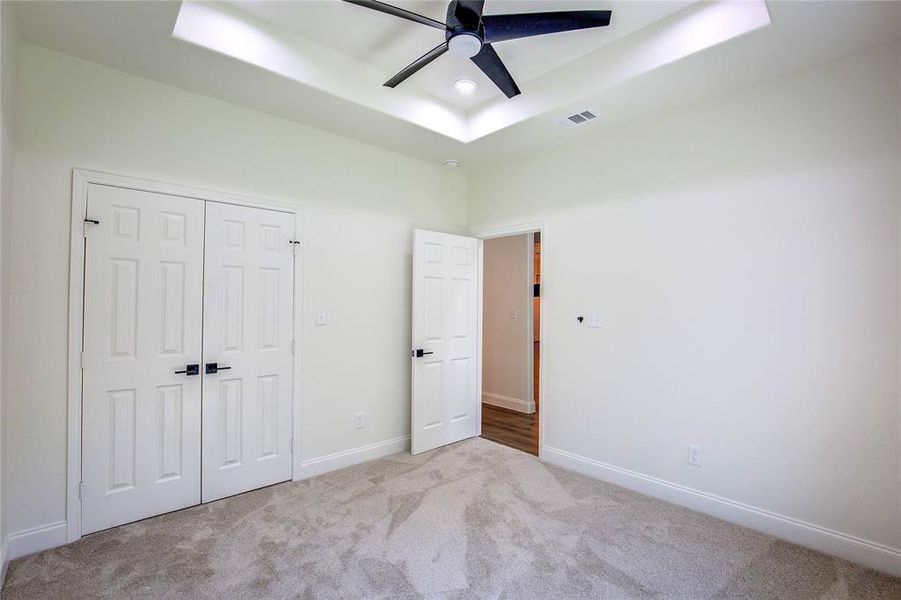 Unfurnished bedroom with carpet, a tray ceiling, a closet, and a ceiling fan Unfurnished bedroom with carpet, a tray ceiling, a closet, and a ceiling fan