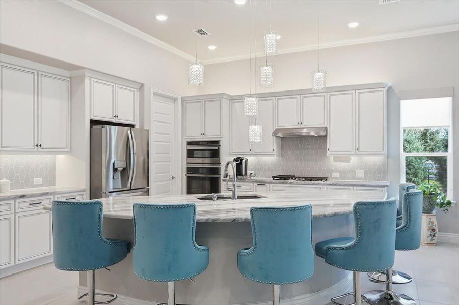 Gourmet kitchen featuring a large curved island with a stone countertop, recessed lighting, pendant lighting, stainless steel appliances, and extensive cabinetry