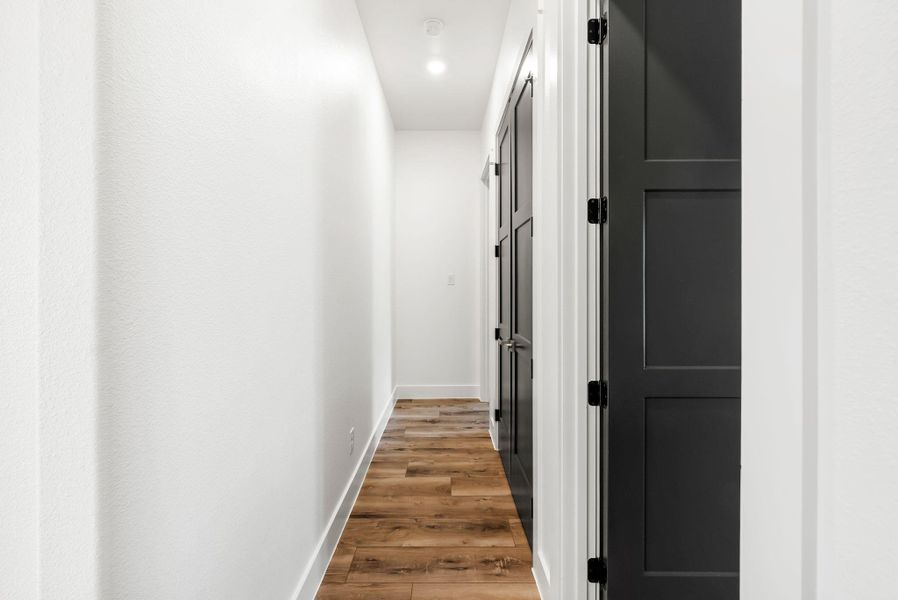 A well-lit hallway with contemporary dark panel doors and rich wood flooring.