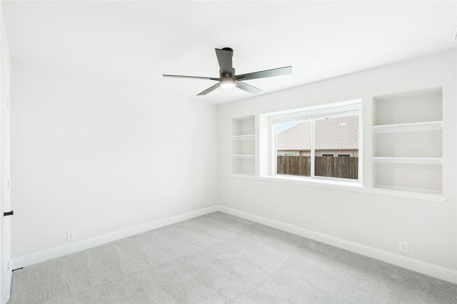 Empty bedroom with carpet, ceiling fan, and built-in shelves flanking a window