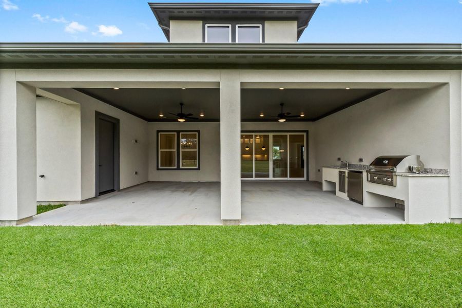 Covered patio with a built-in outdoor kitchen, including a grill and countertop. The area features ceiling fans and is adjacent to a lush green lawn, perfect for entertaining and relaxation. Covered patio with a built-in outdoor kitchen, including a grill and countertop. The area features ceiling fans and is adjacent to a lush green lawn, perfect for entertaining and relaxation.