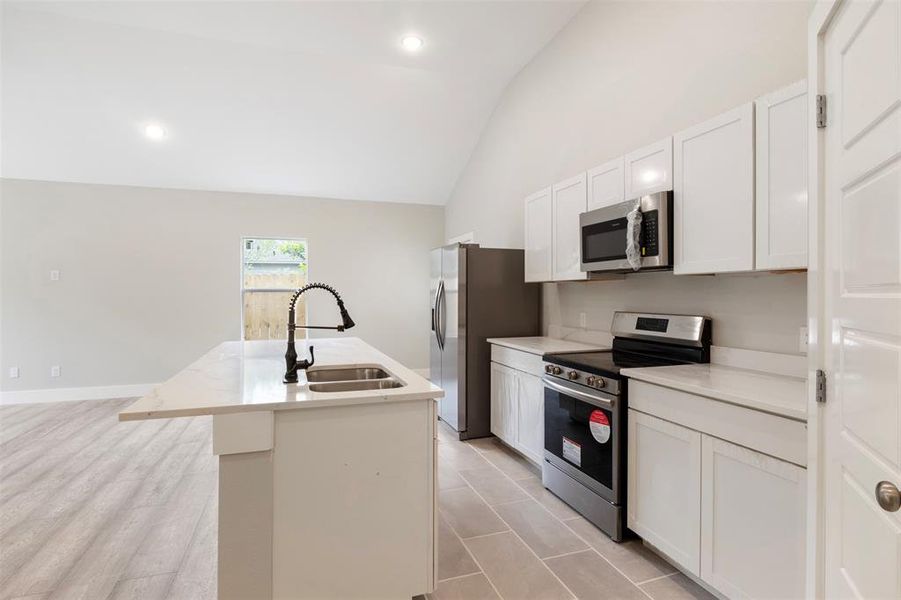 Kitchen with stainless steel appliances, high vaulted ceiling, sink, a kitchen island with sink, and white cabinetry