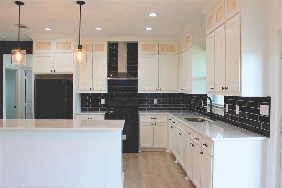 Kitchen featuring wall chimney exhaust hood, black appliances, light stone countertops, decorative backsplash, and light wood finished floors Kitchen featuring wall chimney exhaust hood, black appliances, light stone countertops, decorative backsplash, and light wood finished floors