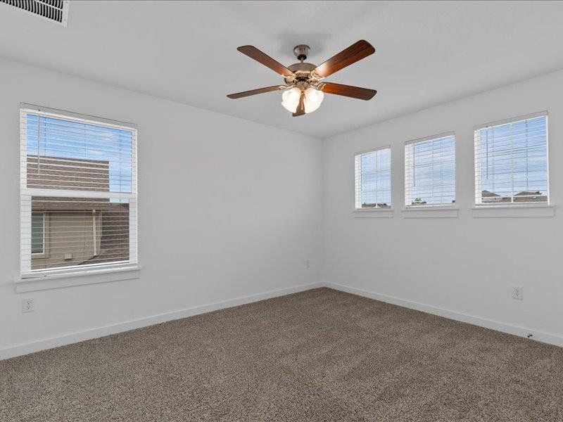 Carpeted empty room featuring plenty of natural light and a ceiling fan
