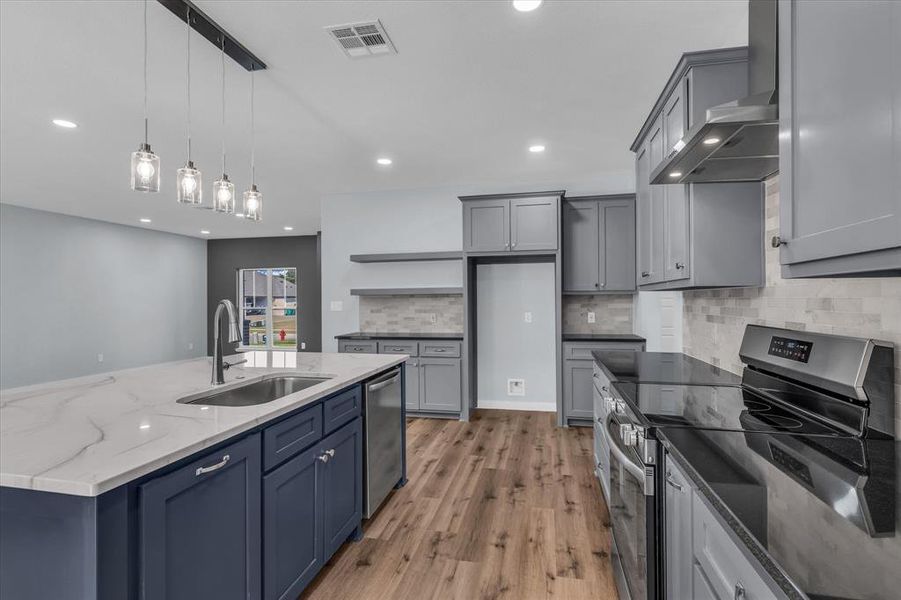 Kitchen featuring stainless steel appliances, pendant lighting, wall chimney exhaust hood, dark stone countertops, and a center island with sink Kitchen featuring stainless steel appliances, pendant lighting, wall chimney exhaust hood, dark stone countertops, and a center island with sink