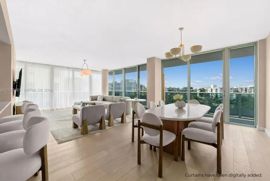 Open-concept living space featuring wood-finish flooring, floor-to-ceiling glass panel walls, and multiple tiered pendant light fixtures Open-concept living space featuring wood-finish flooring, floor-to-ceiling glass panel walls, and multiple tiered pendant light fixtures