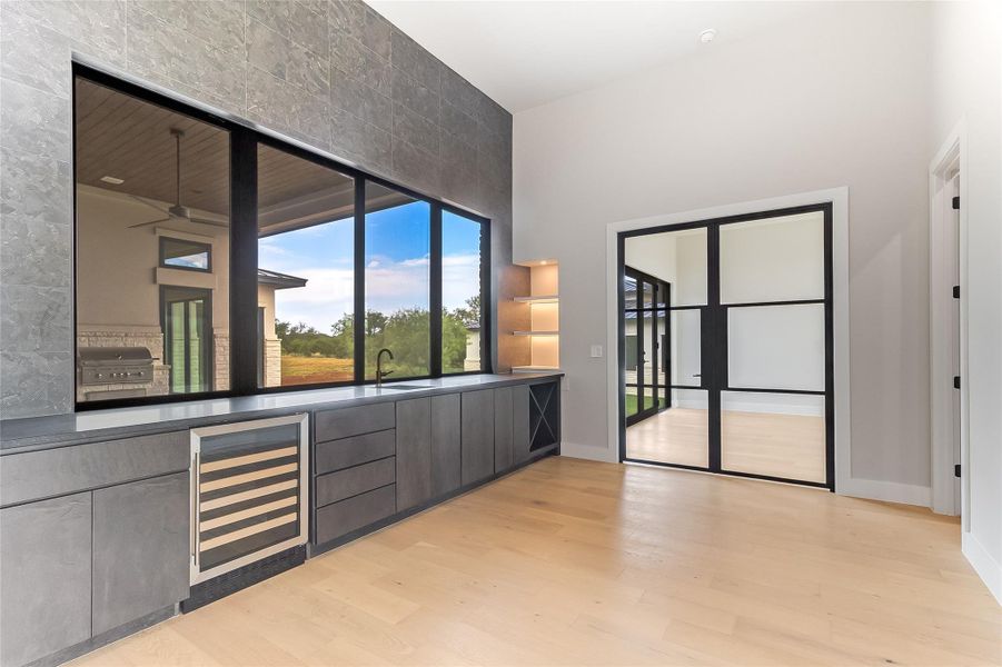 Bar area featuring wine cooler, light wood finished floors, baseboards, a towering ceiling, and a sink Bar area featuring wine cooler, light wood finished floors, baseboards, a towering ceiling, and a sink