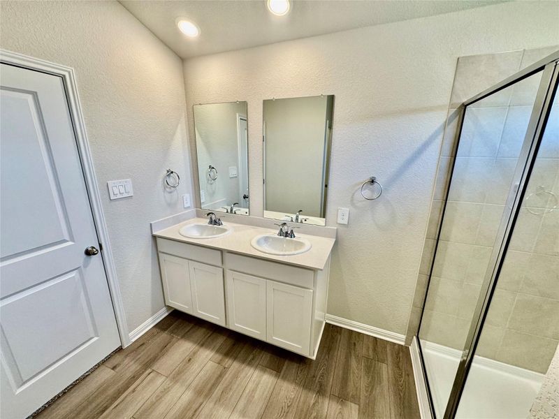 Full bath featuring wood finished floors, a shower stall, double vanity, and a textured wall