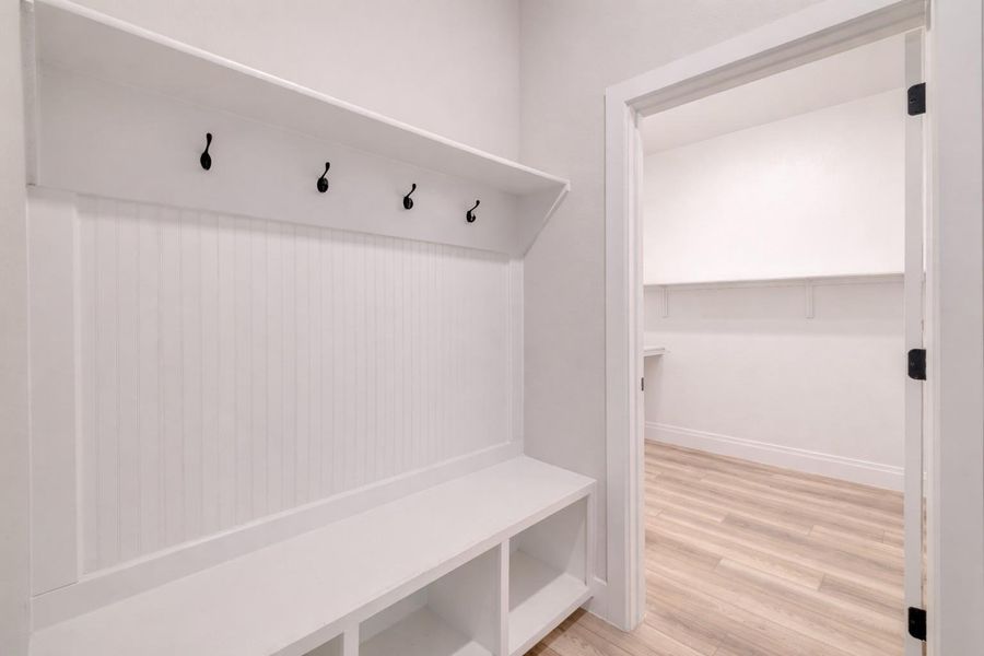 Entryway featuring a built-in bench with storage cubbies, beadboard paneling, and a wall-mounted shelf with five coat hooks