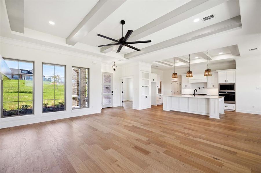 Unfurnished living room featuring ceiling fan, a raised ceiling, sink, and light hardwood / wood-style flooring