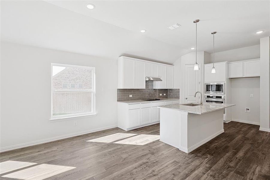 Kitchen with wood-type flooring, stainless steel appliances, white cabinetry, and a center island with sink