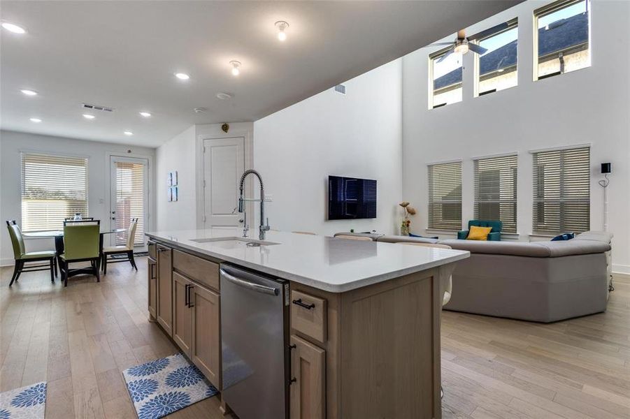 Kitchen with open floor plan, light wood-type flooring, dishwasher, a kitchen island with sink, and light stone counters Kitchen with open floor plan, light wood-type flooring, dishwasher, a kitchen island with sink, and light stone counters