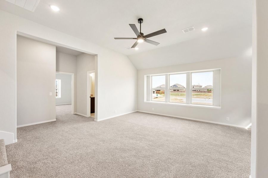 Spacious empty bedroom with vaulted ceiling, ceiling fan, carpet flooring, and large windows Spacious empty bedroom with vaulted ceiling, ceiling fan, carpet flooring, and large windows