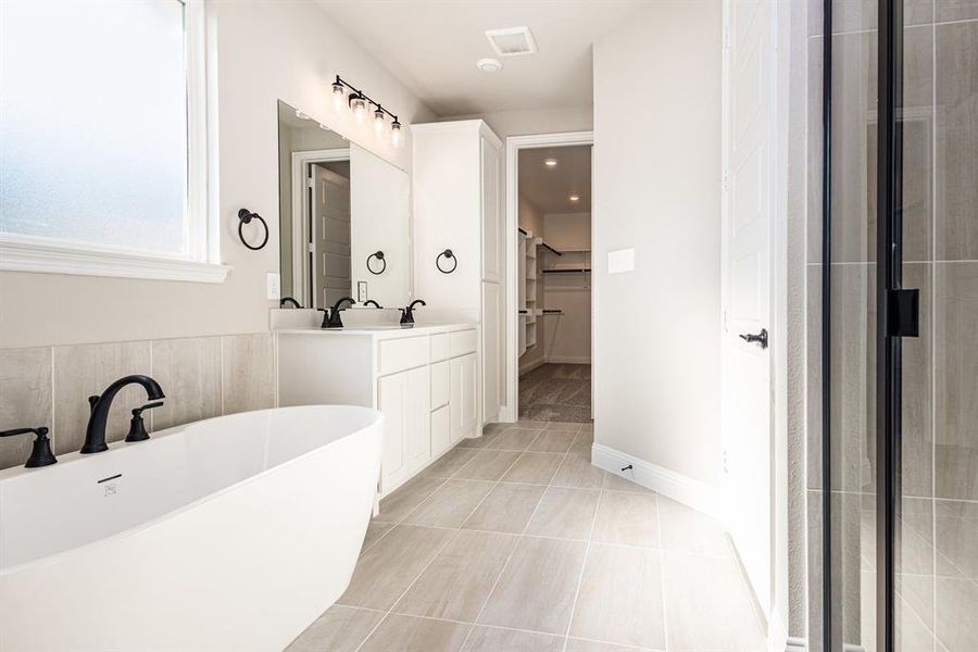 Bathroom with double vanity, a freestanding bath, a walk in closet, and light tile patterned floors