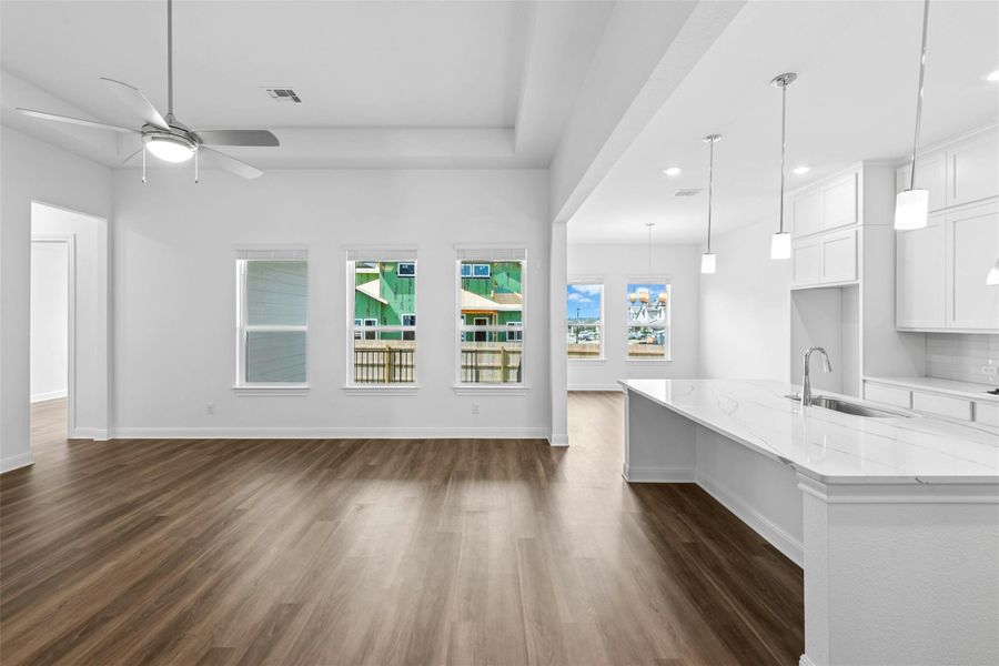 An open-concept living area flows seamlessly into the kitchen, showcasing sleek wood-look flooring and generous natural light.