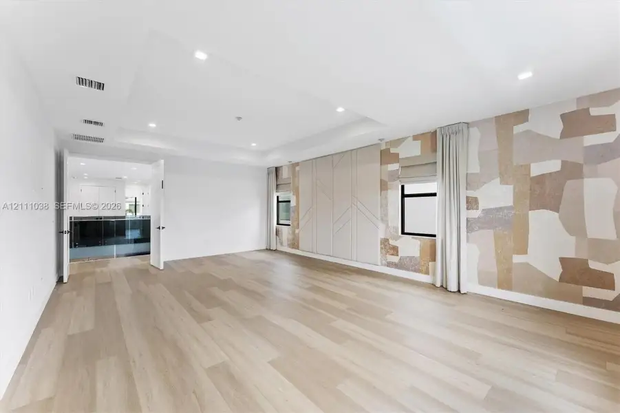 Tray ceiling with recessed lighting, wood-finish flooring, custom geometric wall paneling, and neutral-toned patterned wall covering