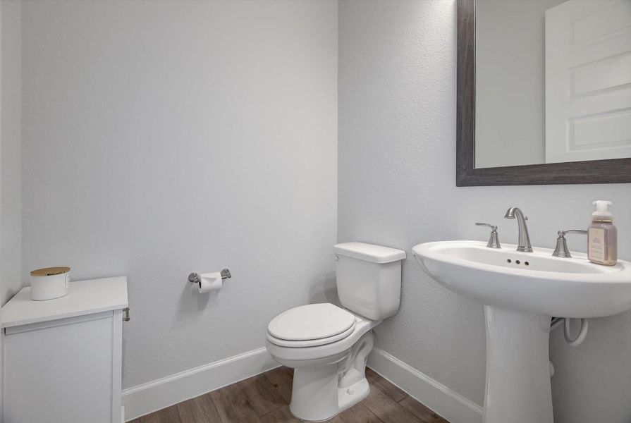 The hallway from the mudroom to the fourth bedroom opens to a roomy half bath, complete with exceptional lighting that enhances the space.  (the cabinet is not staying)