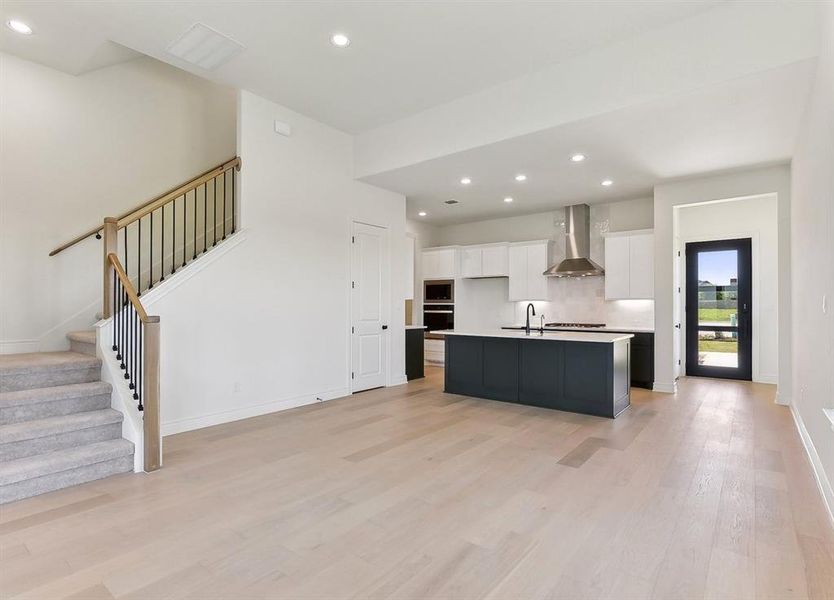 The property features light-colored hardwood flooring, a staircase with a wooden handrail and black balusters, and a modern kitchen with an island, white cabinetry, and stainless steel appliances