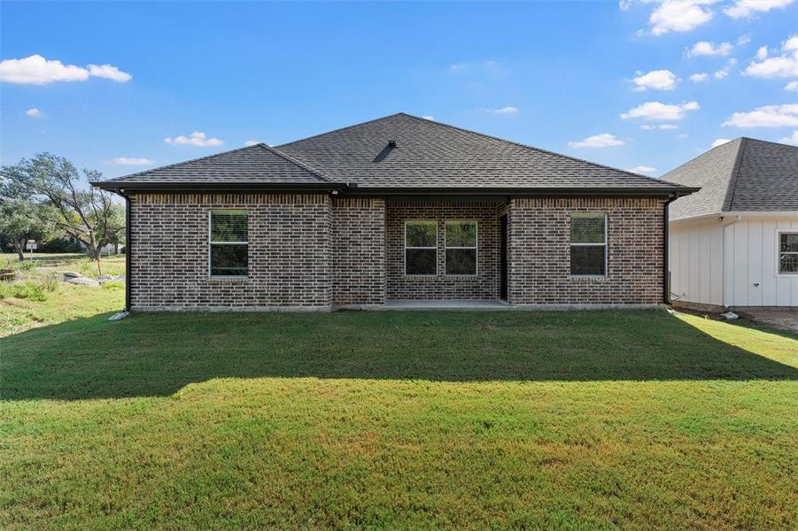 Rear view of house with a patio, a lawn, brick siding, and roof with shingles Rear view of house with a patio, a lawn, brick siding, and roof with shingles