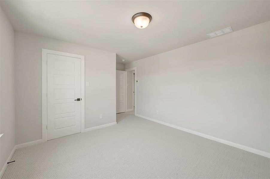 Neutral tone wall paint, light-colored carpet flooring, recessed ceiling light fixture, white five-panel interior door with matte black hardware, and white baseboards
