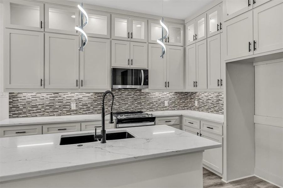 Kitchen with pendant lighting, white cabinets, glass insert cabinets, and light stone countertops