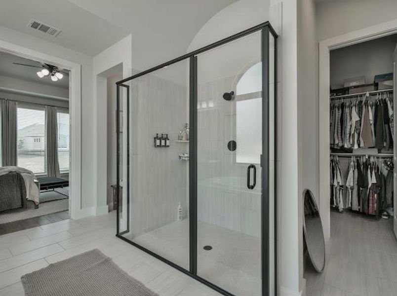Ensuite bathroom featuring a stall shower, light tile patterned flooring, and a spacious closet Ensuite bathroom featuring a stall shower, light tile patterned flooring, and a spacious closet