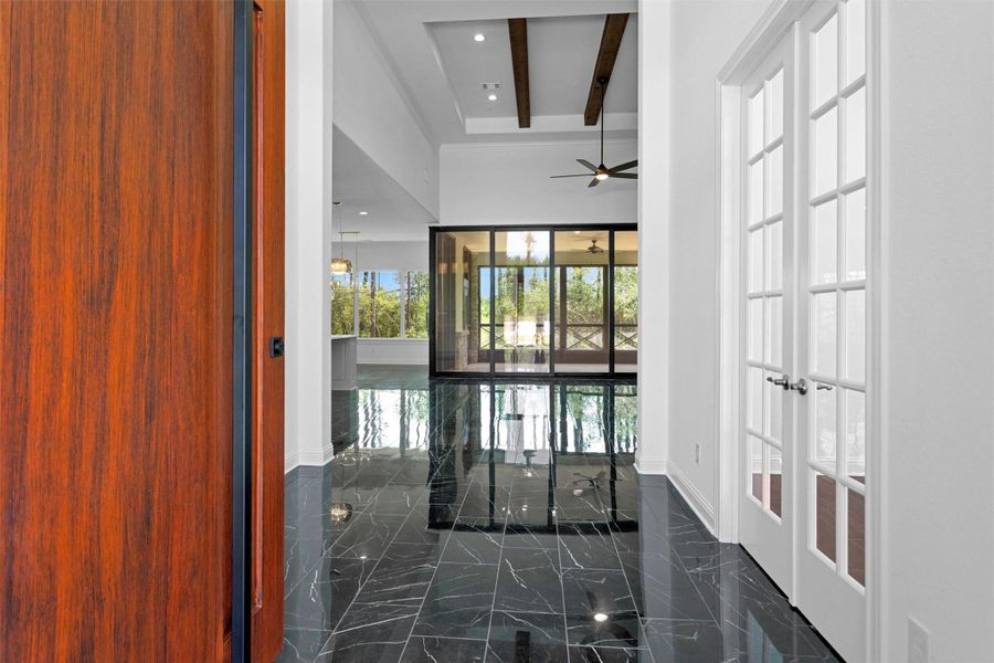 A dramatic entryway sets the tone with sleek black marble tile, soaring ceilings with wood beams, and a wall of glass showcasing serene wooded views beyond the screened patio.