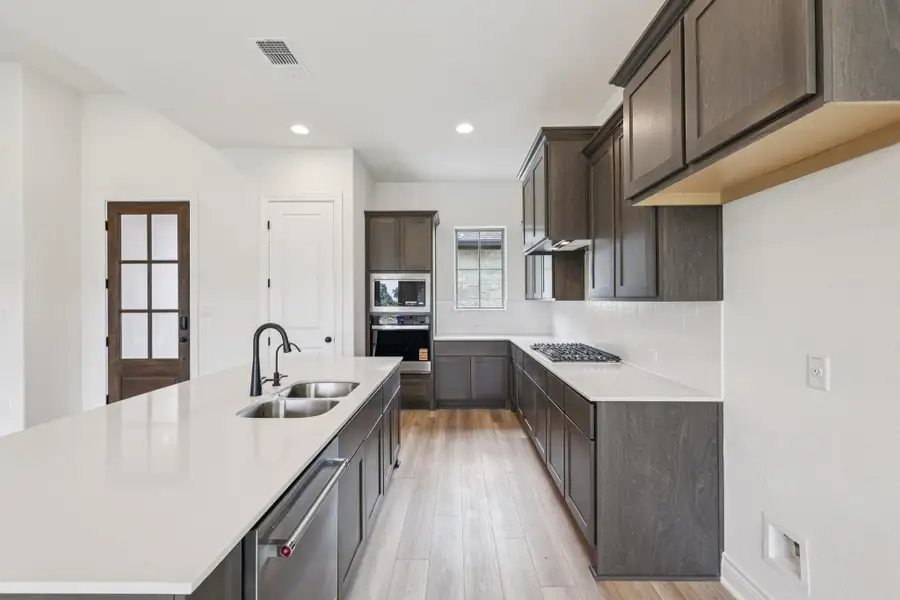Kitchen featuring a center island with sink, recessed lighting, dark brown cabinets, appliances with stainless steel finishes, and light stone counters