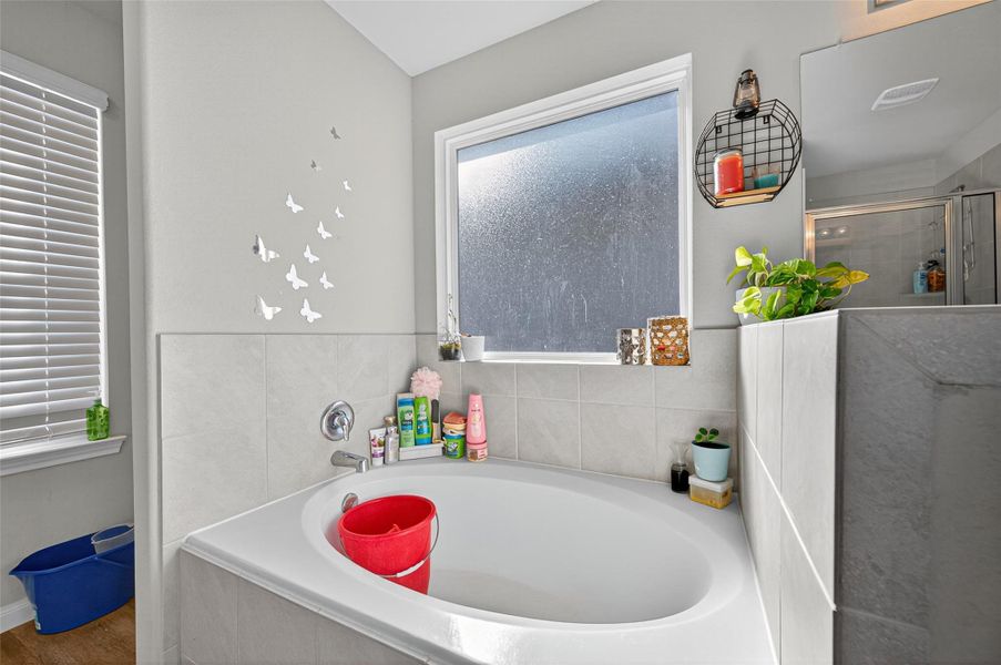 This bathroom features a spacious bathtub set against frosted windows, providing natural light and privacy. The neutral tile design is complemented by decorative accents and shelving, creating a cozy and inviting atmosphere.