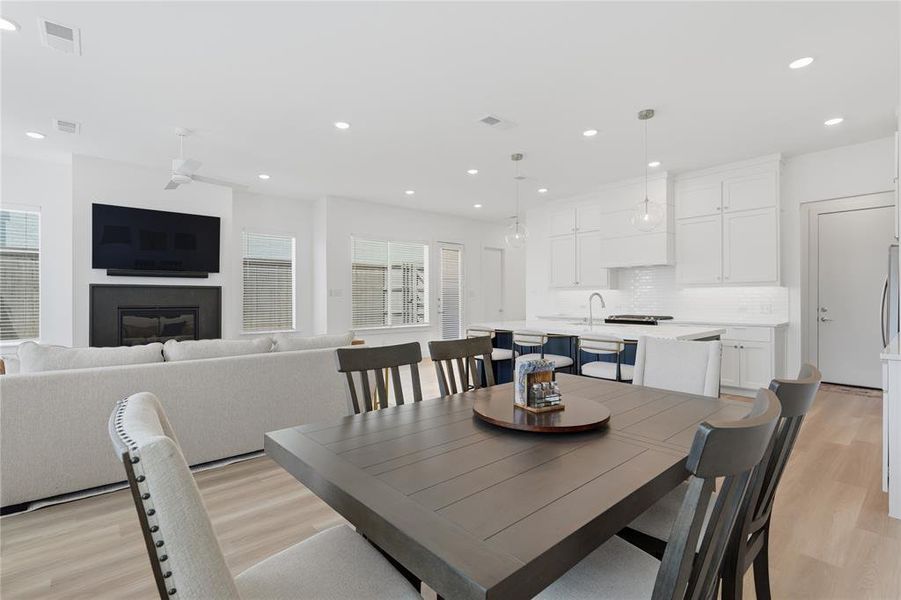 Open-concept living space featuring wood-finish flooring, a contemporary fireplace with dark surround, a kitchen island with seating, white shaker cabinetry, and recessed lighting throughout