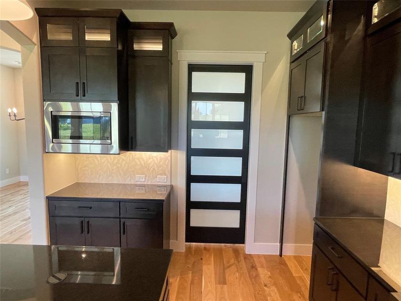 Modern kitchen featuring rich dark cabinetry, stainless steel microwave, stone countertops, and wood-finish flooring