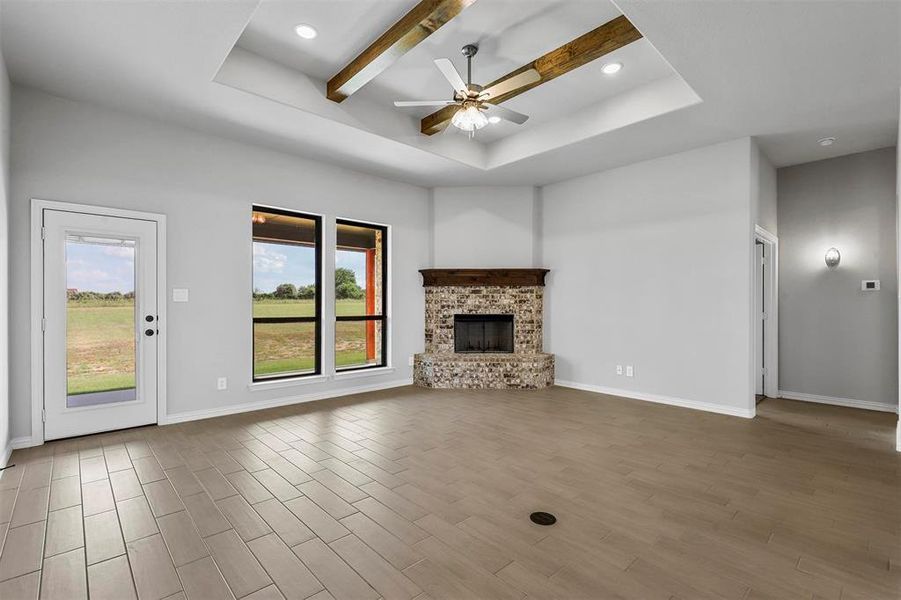 Unfurnished living room featuring beam ceiling, a tray ceiling, ceiling fan, a brick fireplace, and hardwood / wood-style flooring