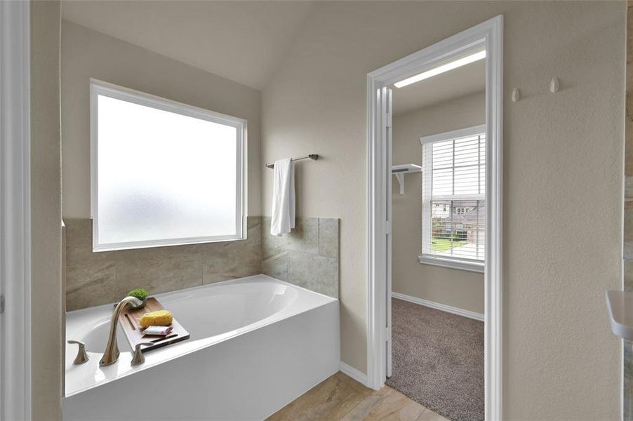 This is a bright, modern bathroom featuring a large soaking tub with tiled surround, frosted window for privacy, and walk in closet. The room has neutral colors providing a serene atmosphere.