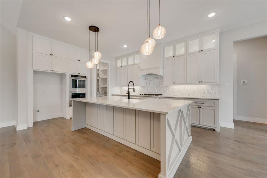 Kitchen featuring white cabinetry, light wood-type flooring, appliances with stainless steel finishes, a kitchen island with sink, and tasteful backsplash