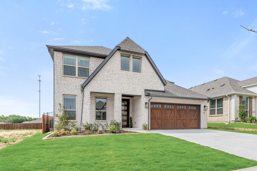 Two-story light brick home with wood garage door, covered entry, and manicured front lawn