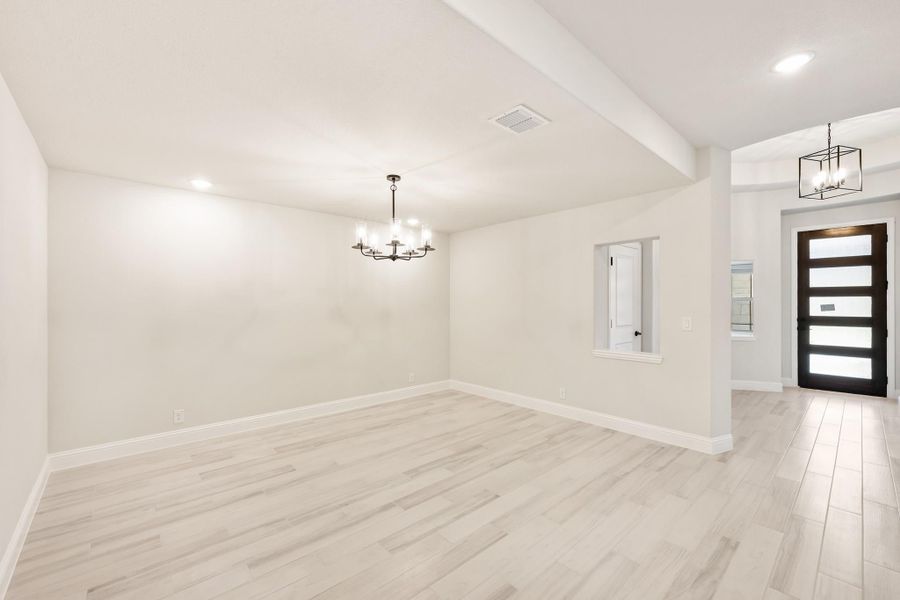 Open living area with light wood floors, chandelier, and modern front entry door Open living area with light wood floors, chandelier, and modern front entry door